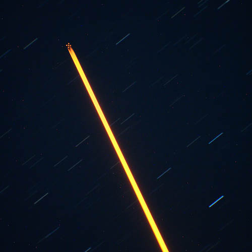 Image of the Gemini South laser guide star system. A constellation-like pattern of artificial stars is seen in the upper left corner. This is created by a laser beam (visible as a yellow-orange streak) shining towards the sky.