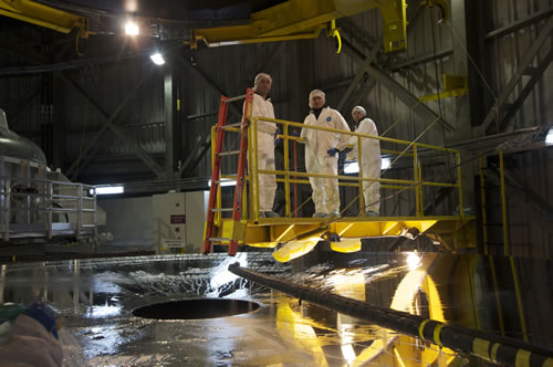 Photo of Claudio Araya, Christian Aguilar, and Hector Figueroa standing on the wash bridge during the initial phase of stripping the old coating off of the Gemini North telescope's primary mirror.